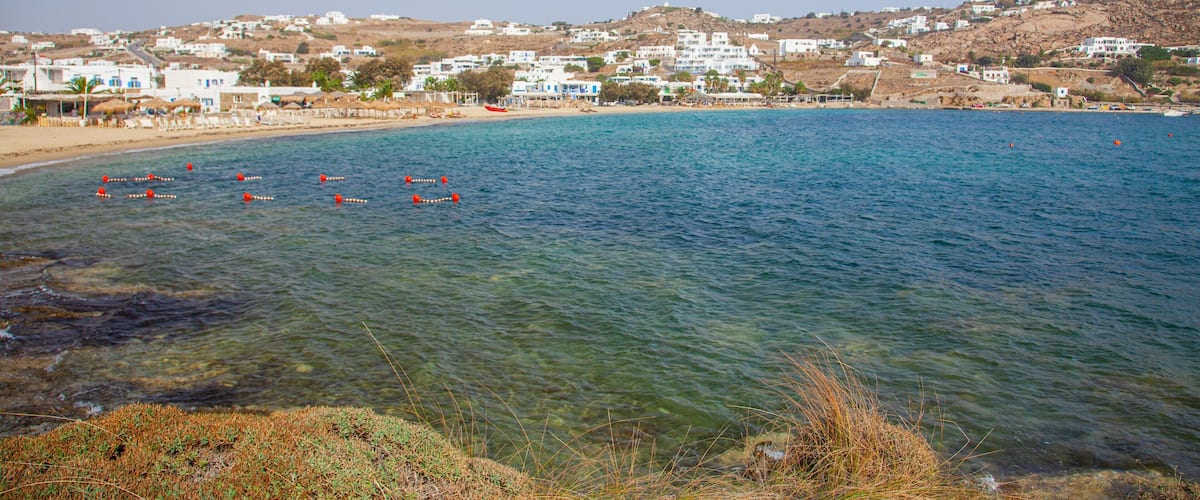 A coastal town with clear blue waters, a sandy beach, and white buildings on a hillside.