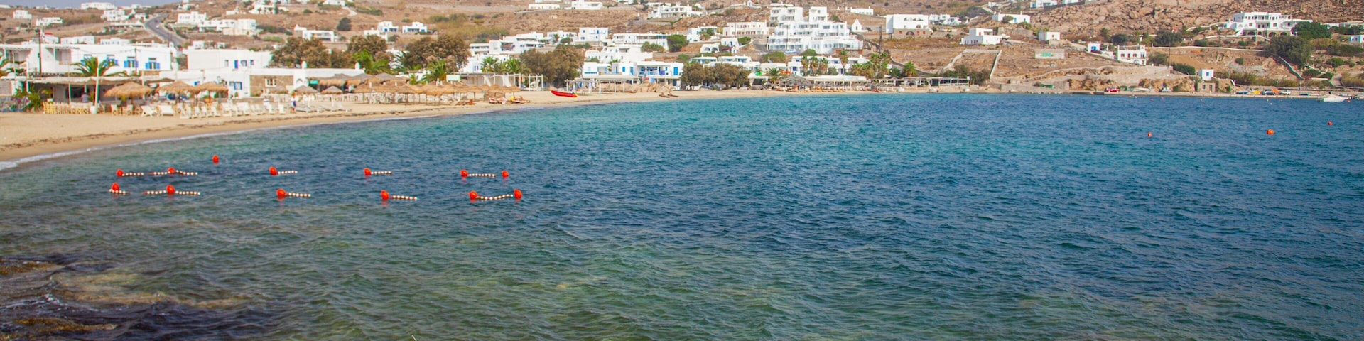 A coastal town with clear blue waters, a sandy beach, and white buildings on a hillside.