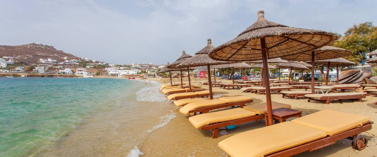 A beach with sun loungers and thatched umbrellas.