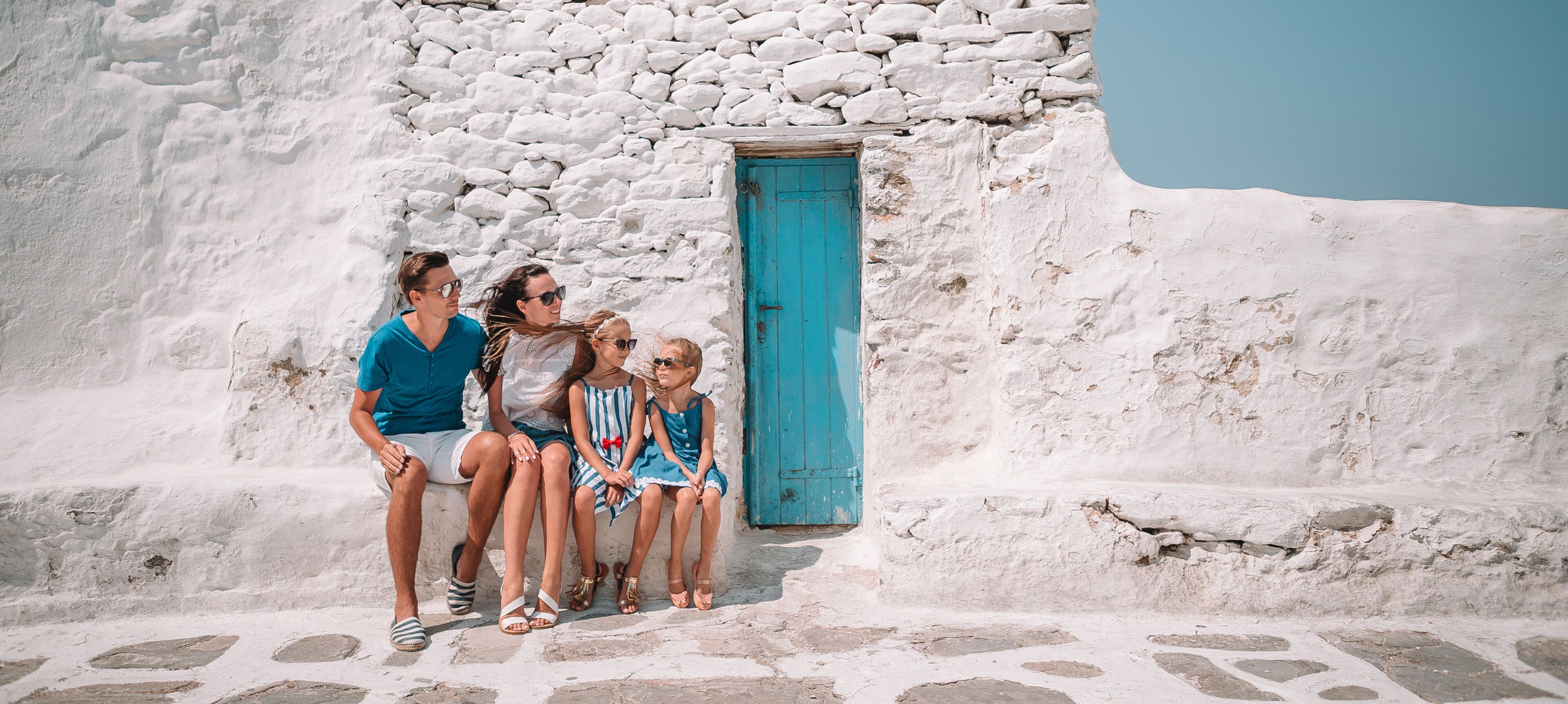 A family sitting against a whitewashed building with a blue door.