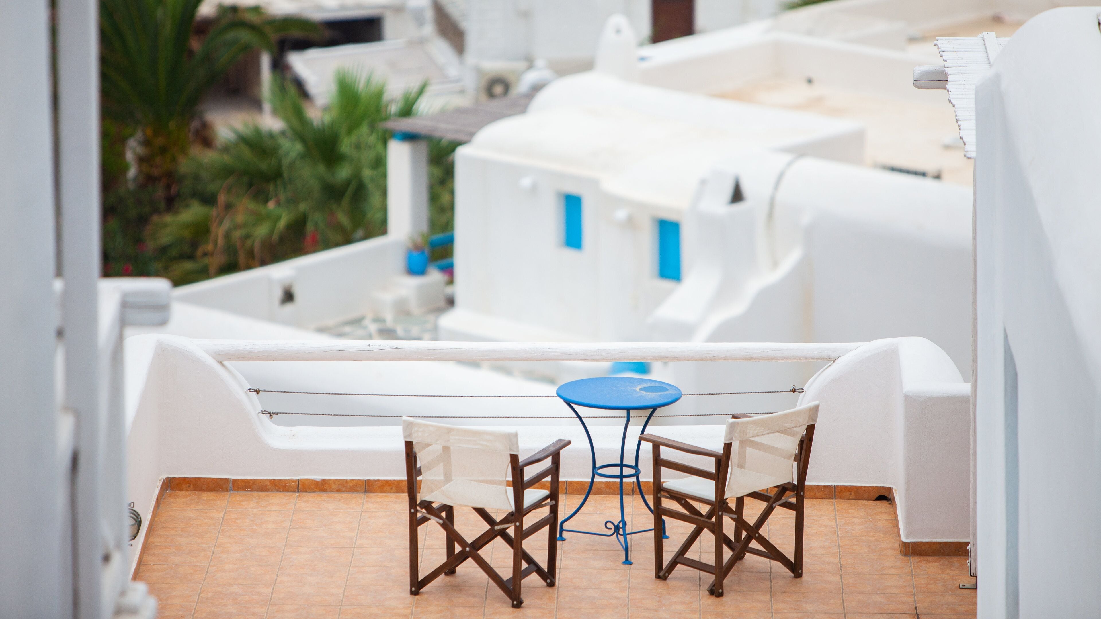 A white outdoor terrace with a blue table and two wooden chairs.