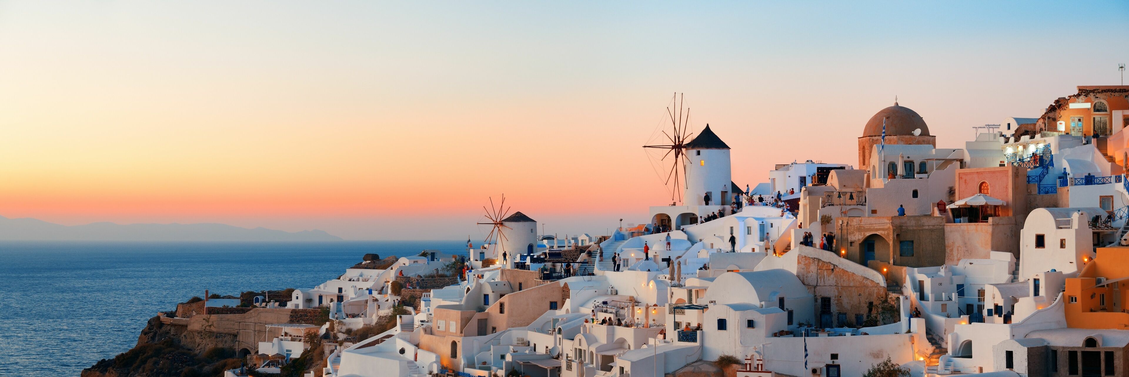 A coastal town with white buildings, windmills, and a sunset over the sea.