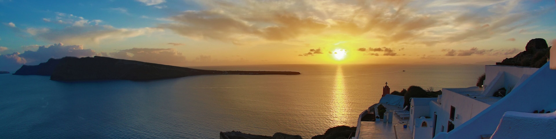Pôr do sol costeiro com edifícios brancos e céu limpo.