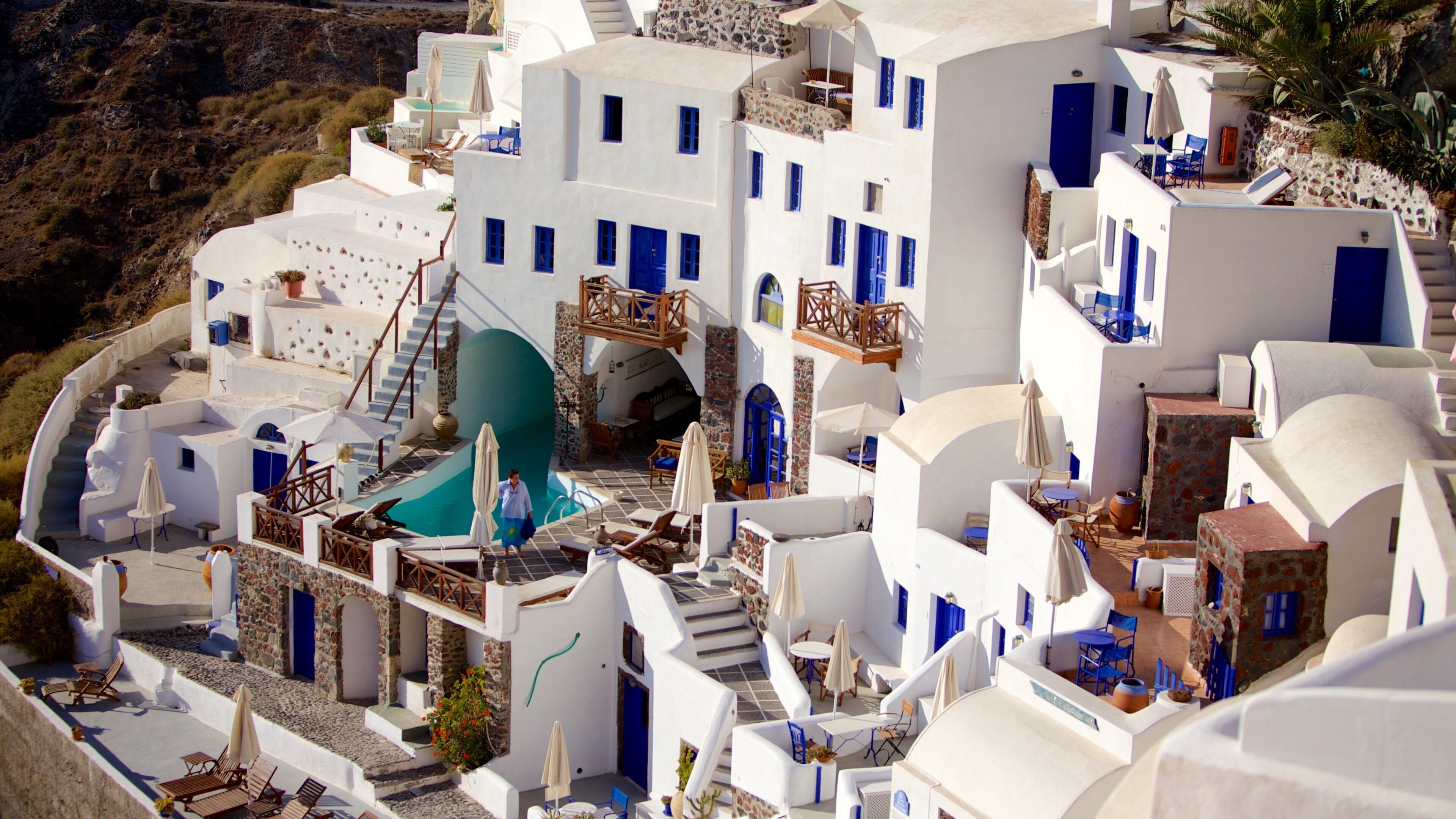A white-washed village with blue doors and windows, a pool, and a staircase leading to a rooftop.