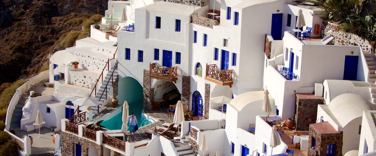 A white-washed village with blue doors and windows, a pool, and a staircase leading to a rooftop.