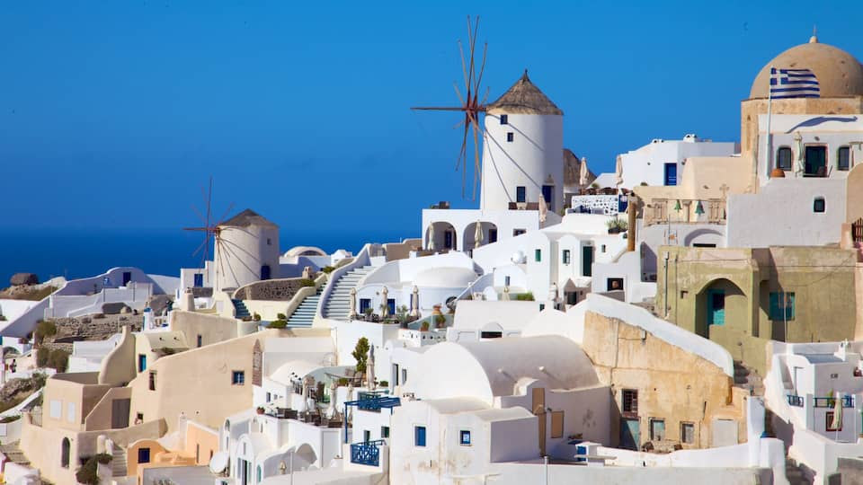 A coastal village with white-washed buildings, a prominent windmill, and a clear blue sky.
