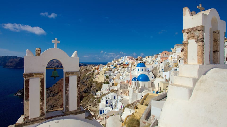 A coastal town with white-washed buildings, blue domes, and a clear blue sky.