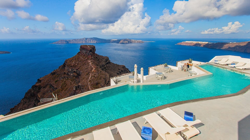 A clear blue pool with lounge chairs and umbrellas, overlooking a rugged coastline and the sea.
