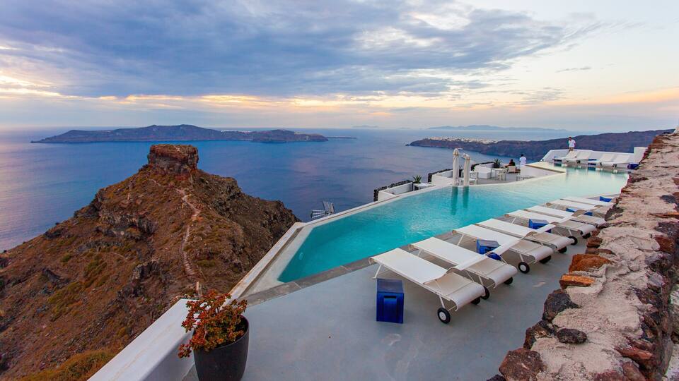 A pool with lounge chairs overlooking a scenic view of the sea and islands.