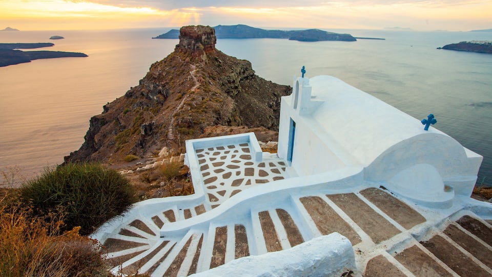 A white-washed staircase leading to a cliff overlooking a calm sea with distant islands.