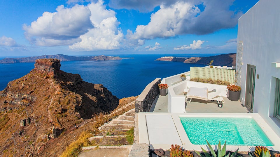 A white building with a pool overlooking a cliff and the sea.
