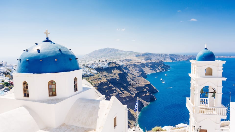White buildings with blue domes, a clear blue sea, and rocky cliffs.
