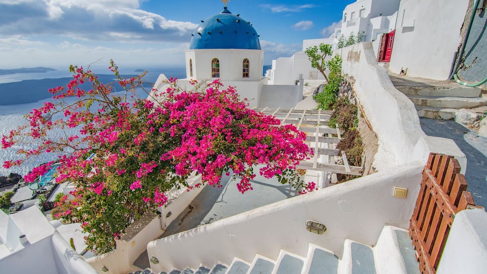 A white-washed building with a blue dome, pink bougainvillea, and a red door.