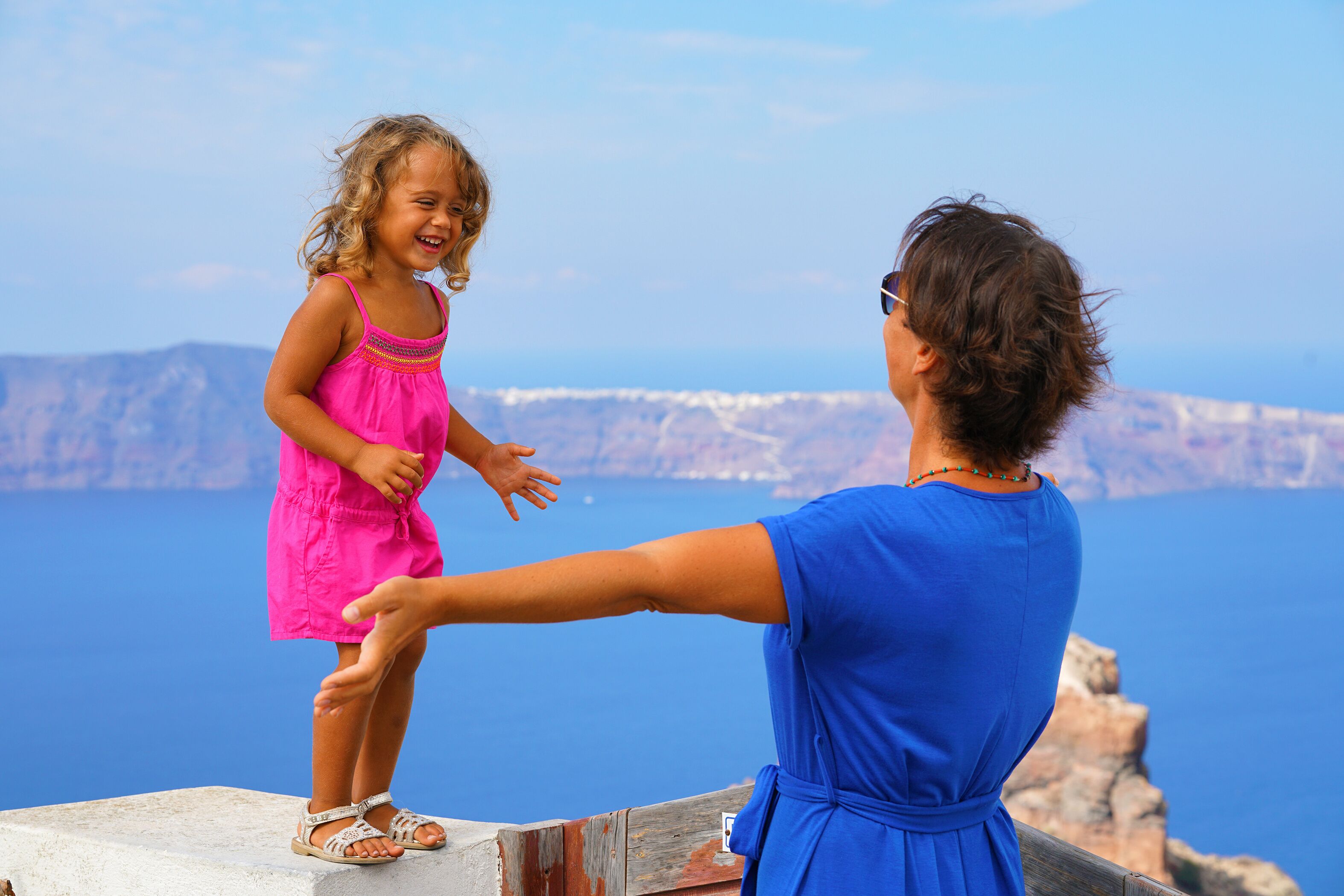Una mujer y un niño en un acantilado con vistas a un cuerpo de agua y montañas al fondo.