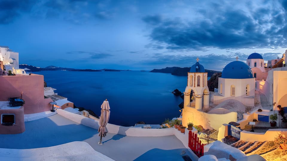 A coastal village with white-washed buildings, blue domes, and a view of the sea.