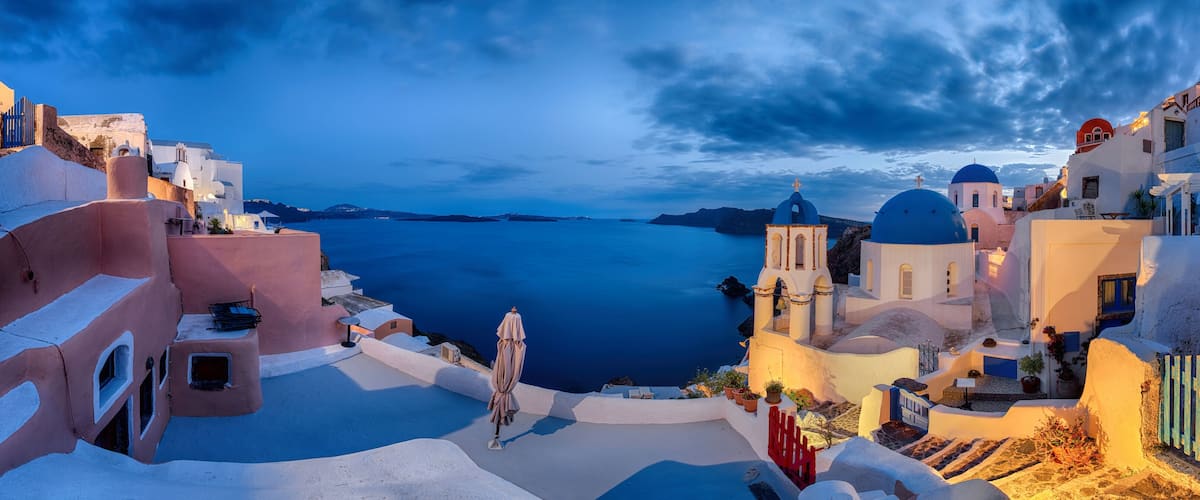 A coastal village with white-washed buildings, blue domes, and a view of the sea.