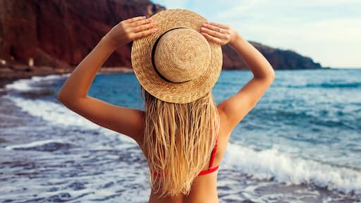Sexy woman in bikini relaxing on Red beach in Santorini, Greece. Girl enjoying sea and mountain landscape