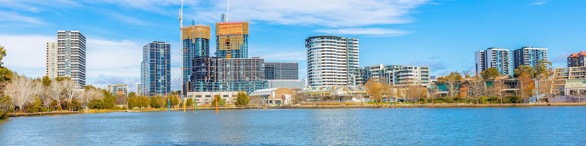 A city skyline with modern high-rise buildings and a body of water in the foreground.