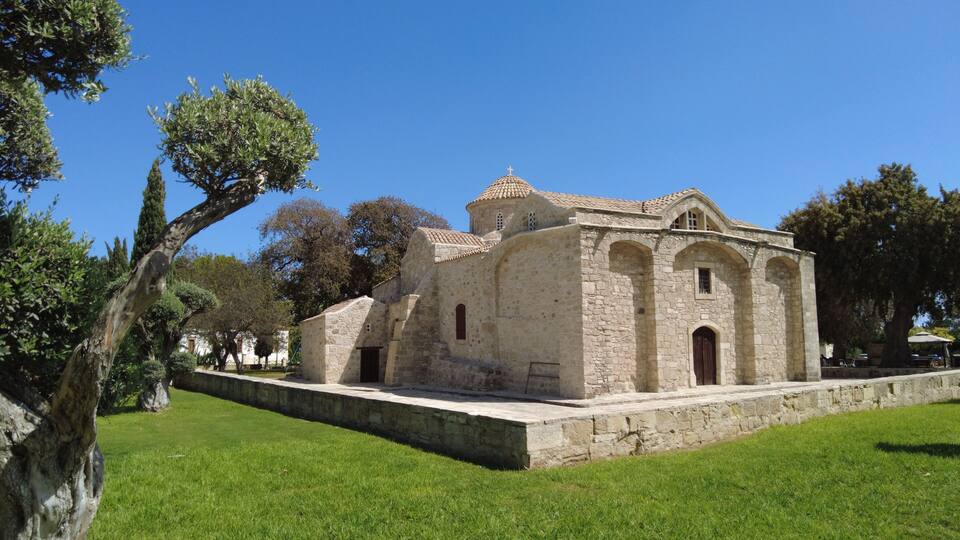 A historic stone building with a cross on top, surrounded by a well-maintained lawn and trees.