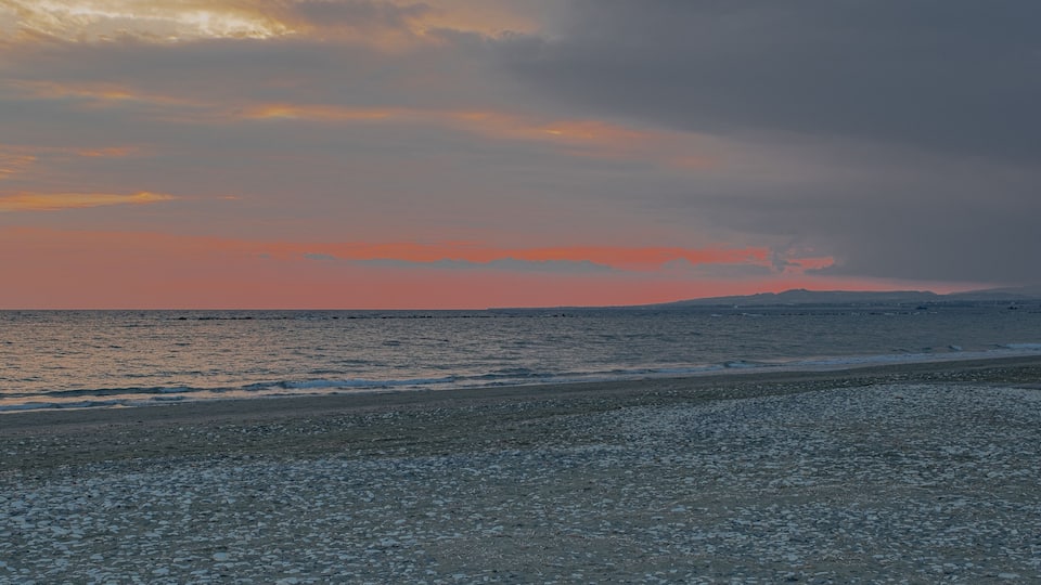 A beach with pebbles and a sunset over the ocean.