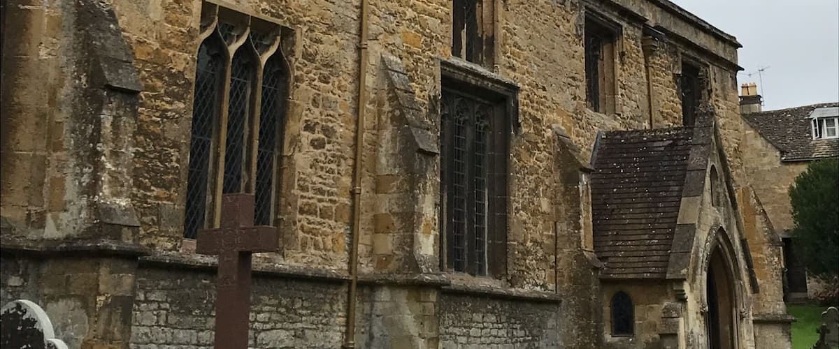 A historic stone building with a clock tower, arched windows, and a grassy courtyard.