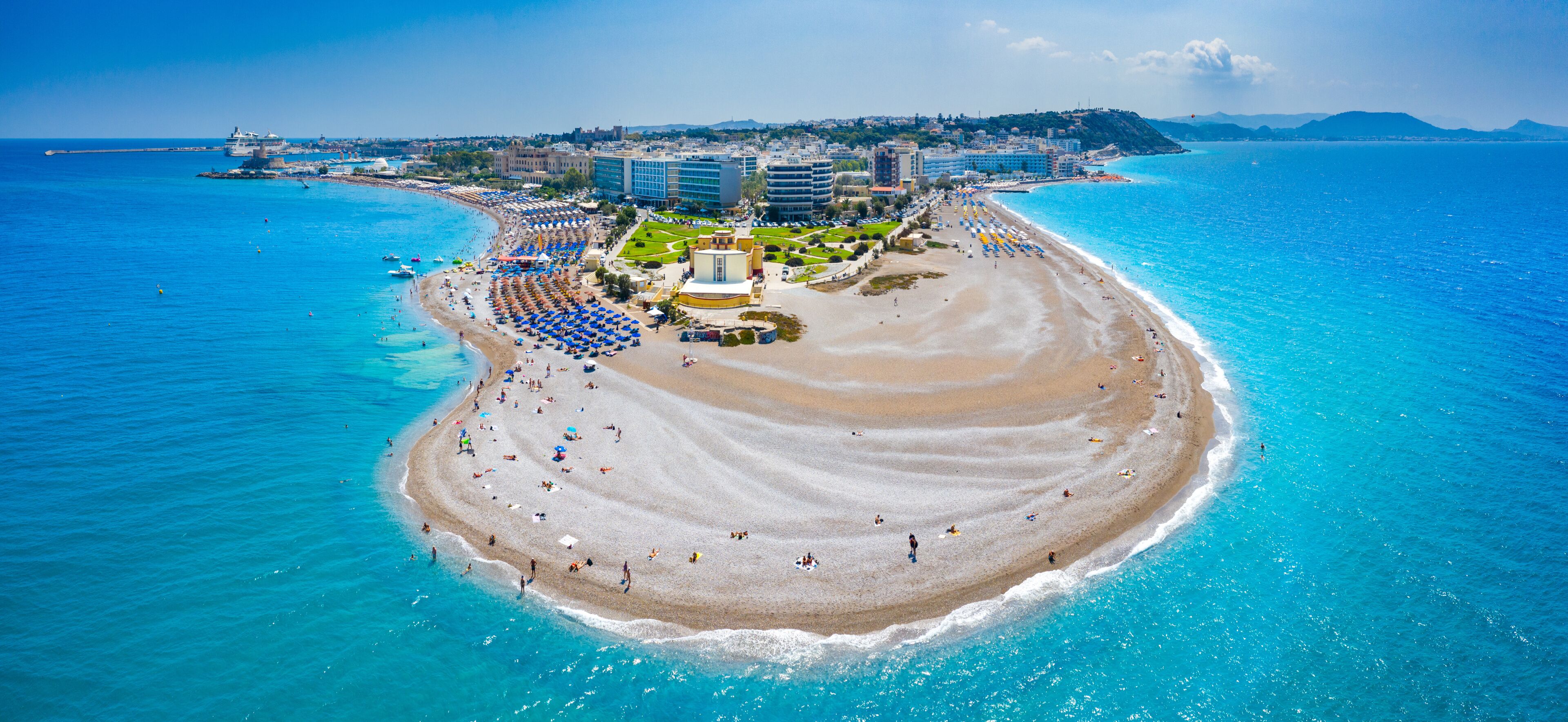 A coastal cityscape with a wide beach, clear blue waters, and a prominent hotel complex.