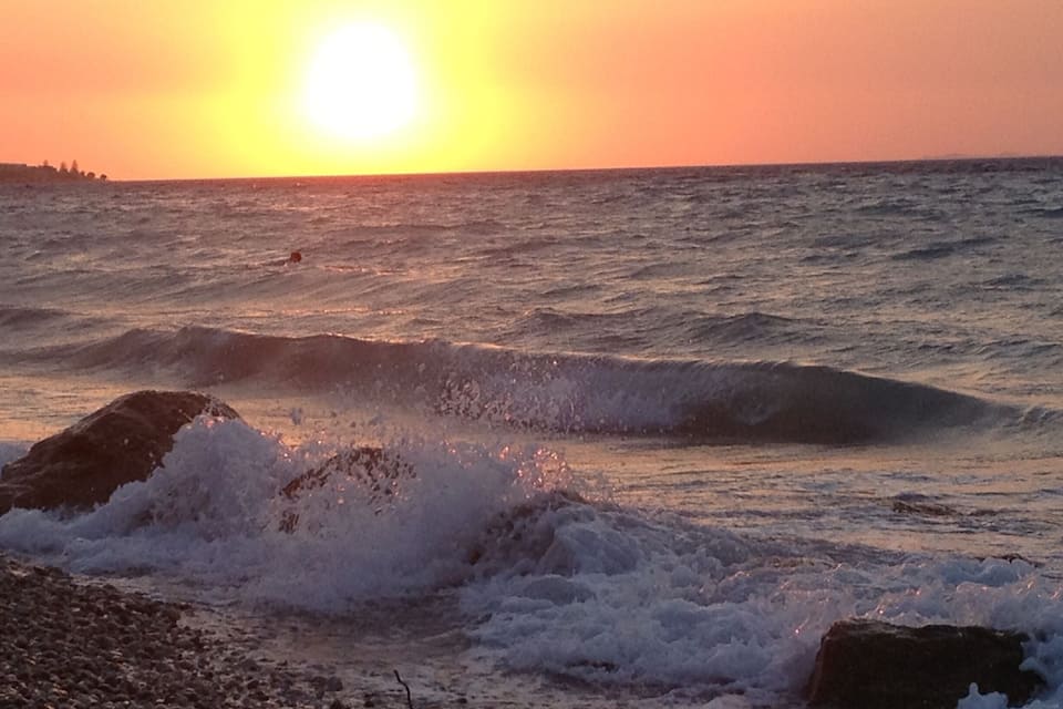 A sunset over the ocean with waves crashing onto a rocky shore.
