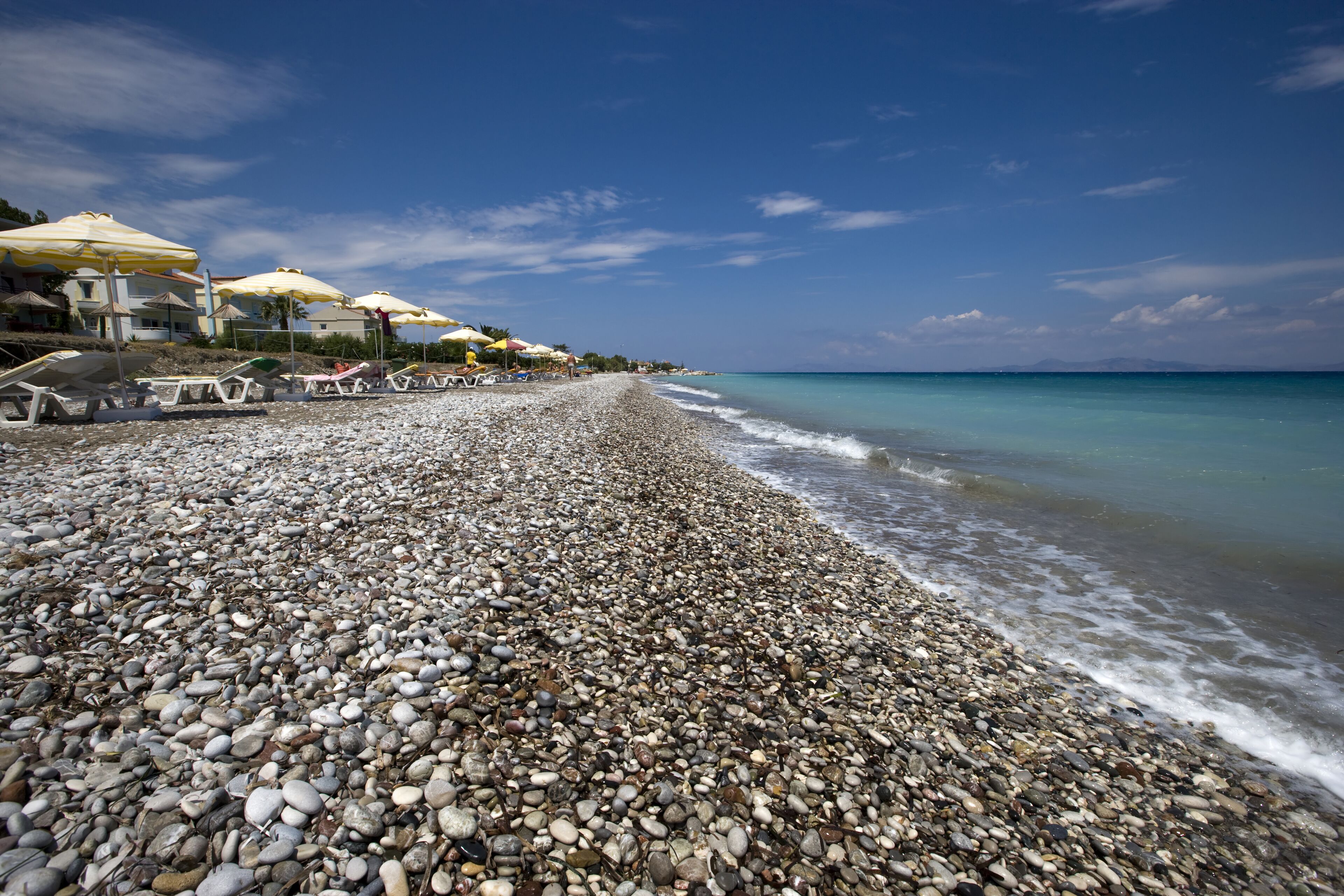 A pebbled beach with umbrellas and lounge chairs.
