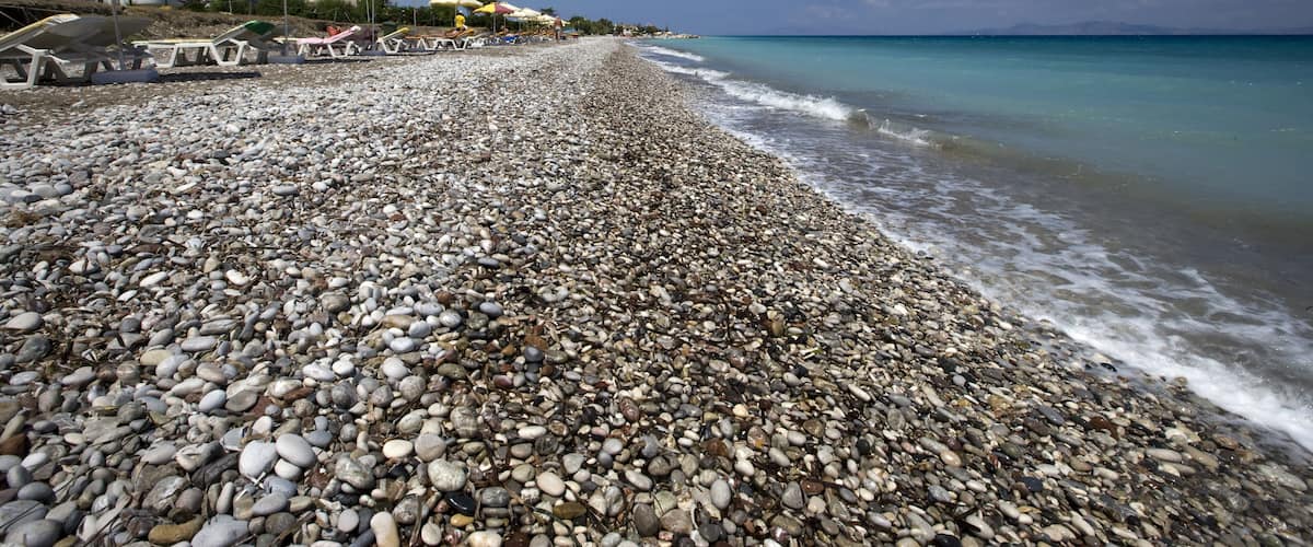 A pebbled beach with umbrellas and lounge chairs.