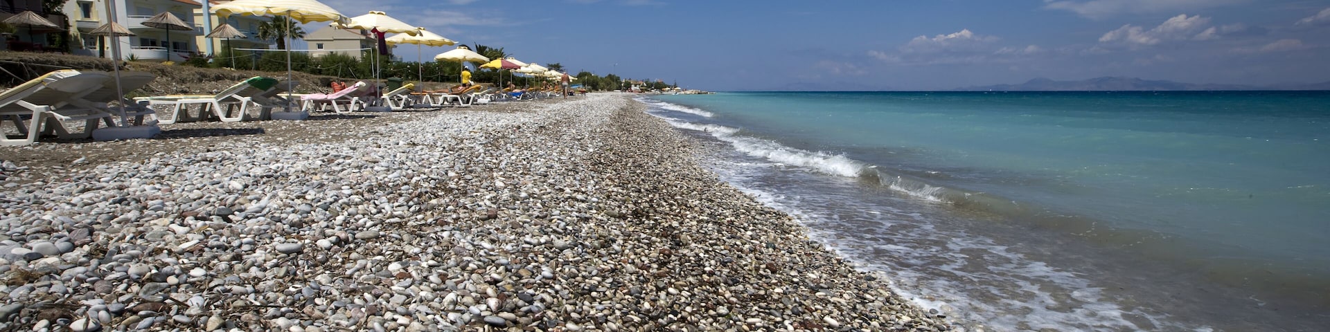 A pebbled beach with umbrellas and lounge chairs.