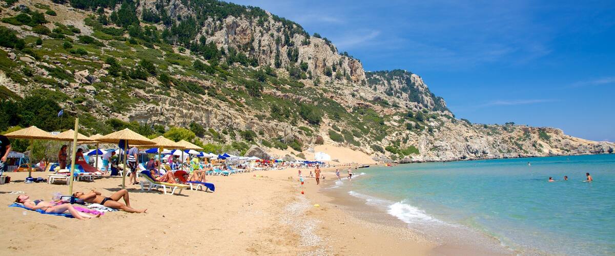 A beach with people sunbathing, umbrellas, and a rocky cliff in the background.