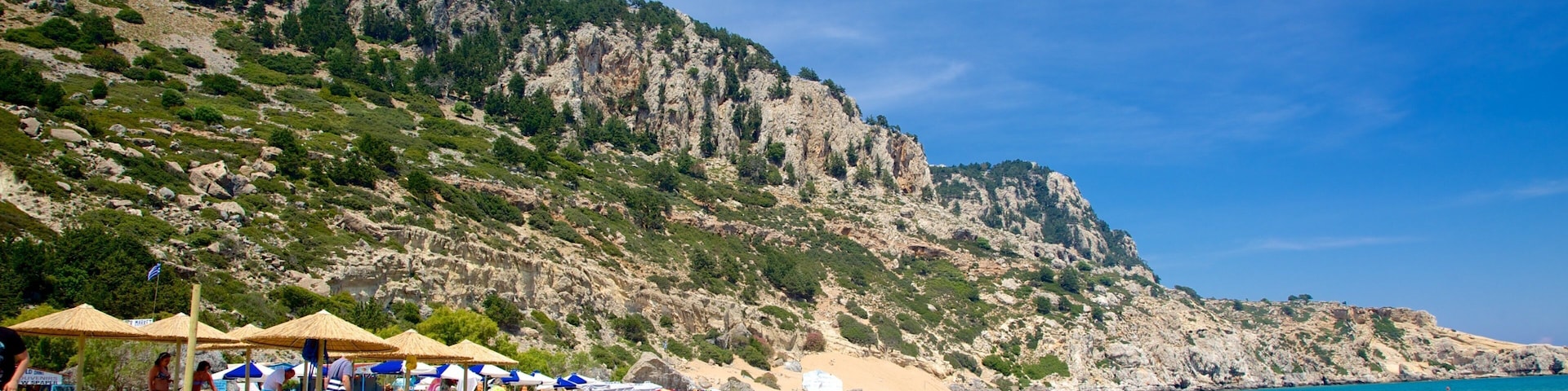 A beach with people sunbathing, umbrellas, and a rocky cliff in the background.