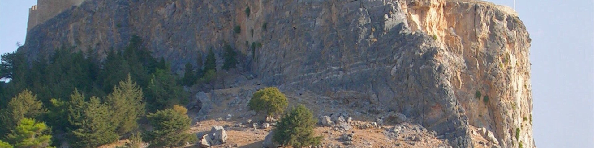 Une colline rocheuse surmontée d’une structure fortifiée, entourée d’une végétation clairsemée.