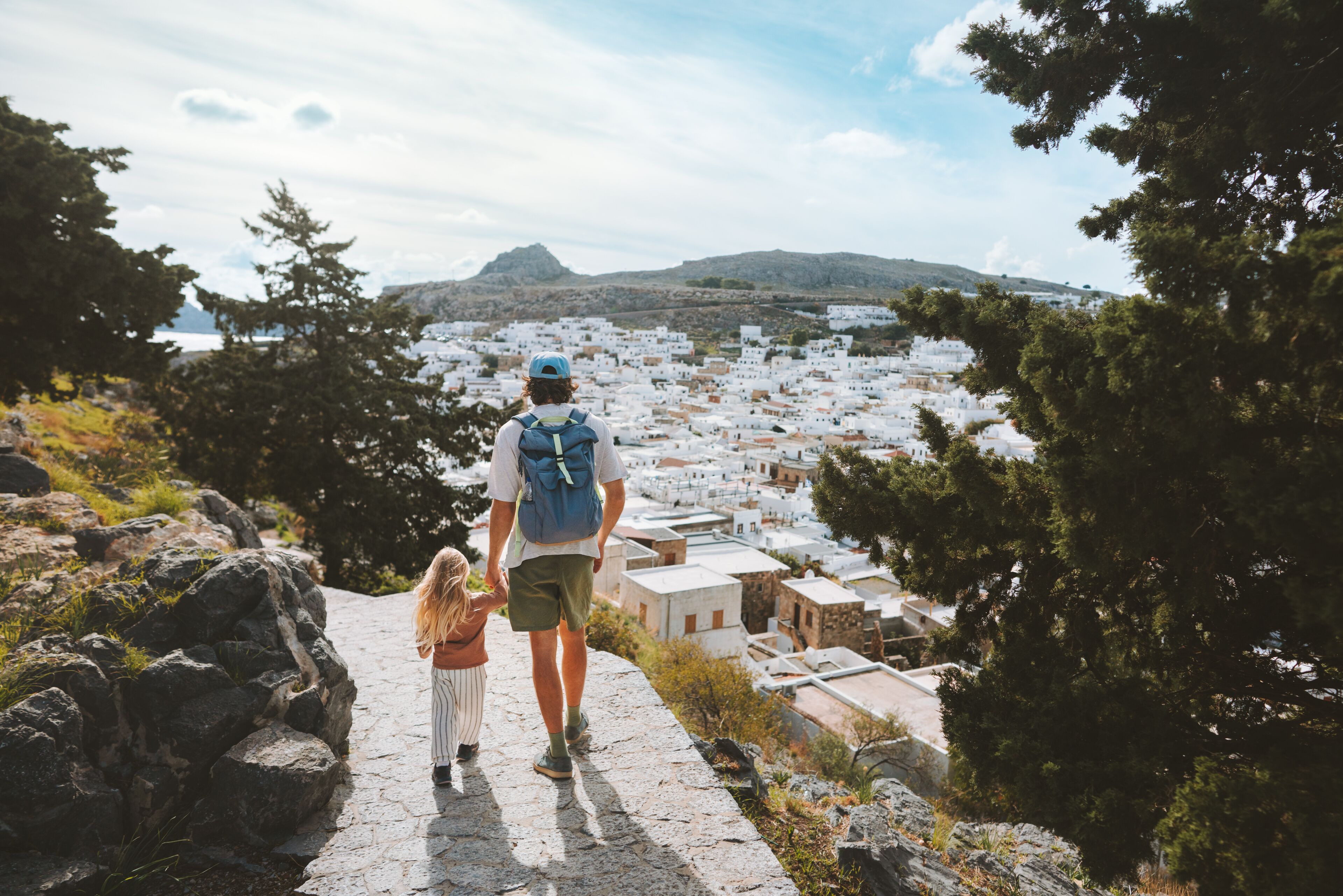Un hombre y un niño caminando por un sendero de piedra con un paisaje montañoso al fondo.