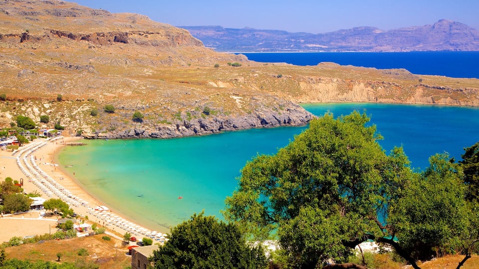 A coastal landscape with a turquoise bay, rocky cliffs, and a beach with umbrellas.