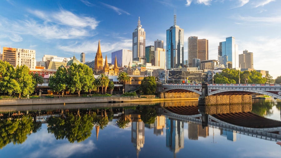 A city skyline with a prominent cathedral, modern skyscrapers, and a bridge over a reflective river.