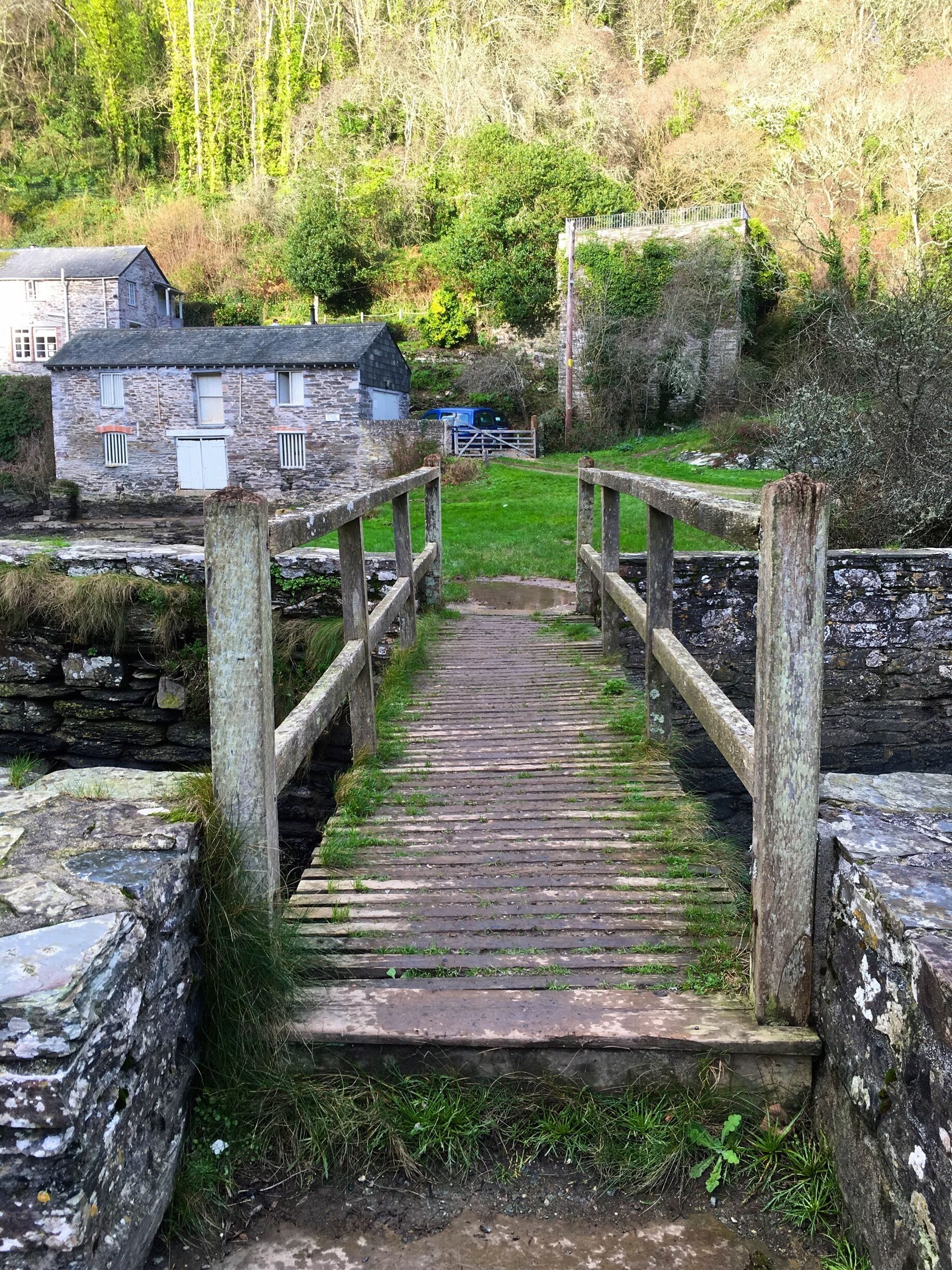 A wooden bridge leading to a stone building with a thatched roof.