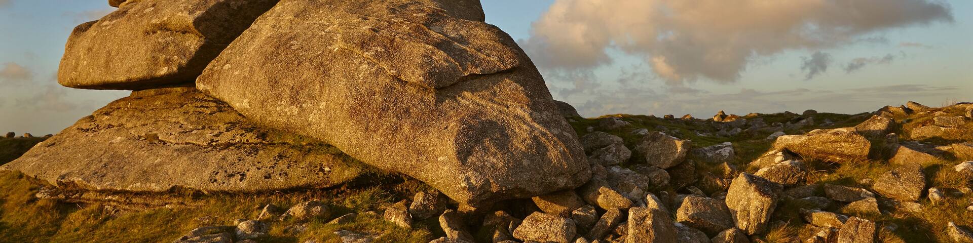 A stack of large boulders on a grassy field with a clear sky.
