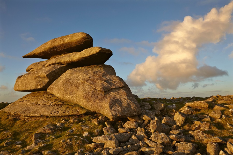 A stack of large boulders on a grassy field with a clear sky.