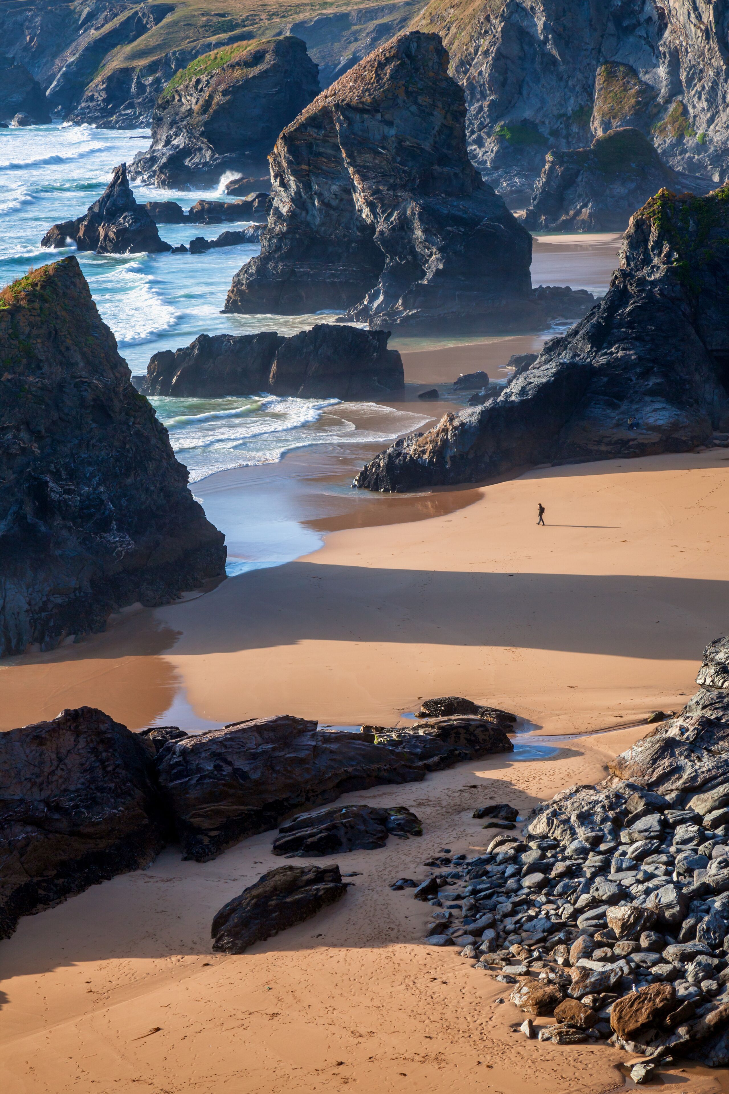 Bedruthan Steps and beach at low tide on the North Cornwall coast, with the late afternoon summer sun casting long shadows.