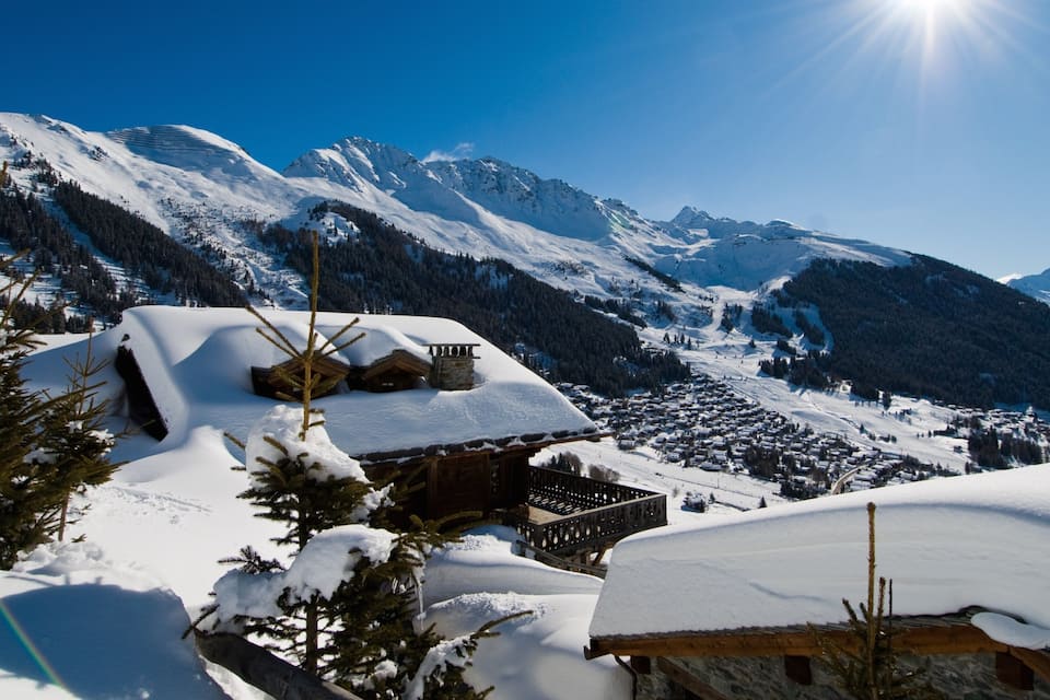 A snow-covered mountain village with wooden houses and pine trees.