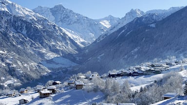 A snow-covered mountain village nestled in a valley with steep, snow-capped peaks in the background.