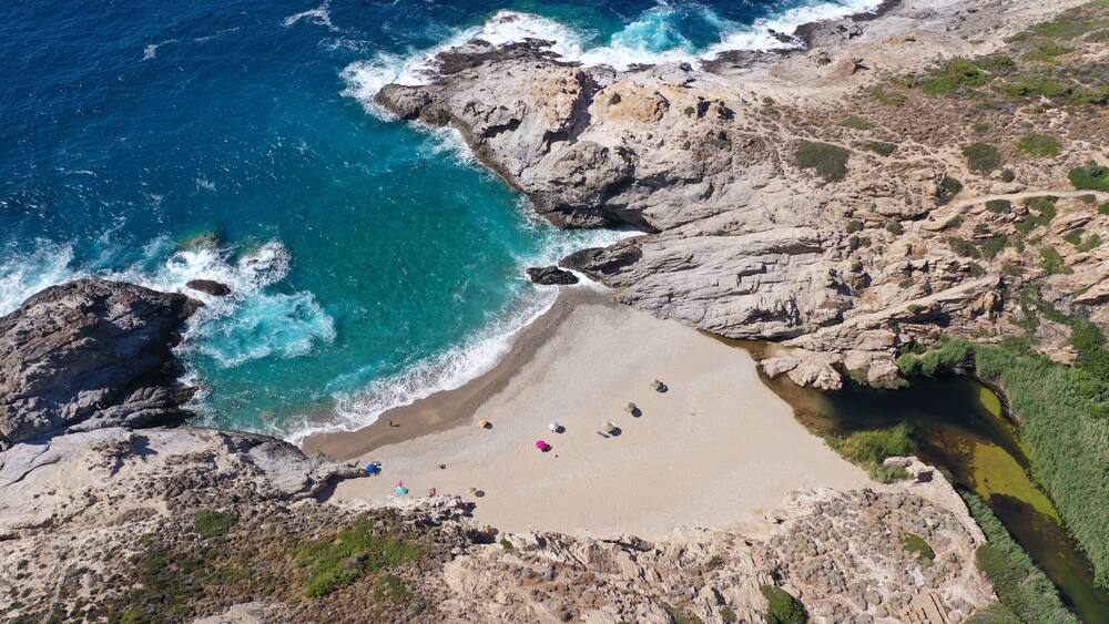 A rocky coastline with a sandy beach and clear blue waters.