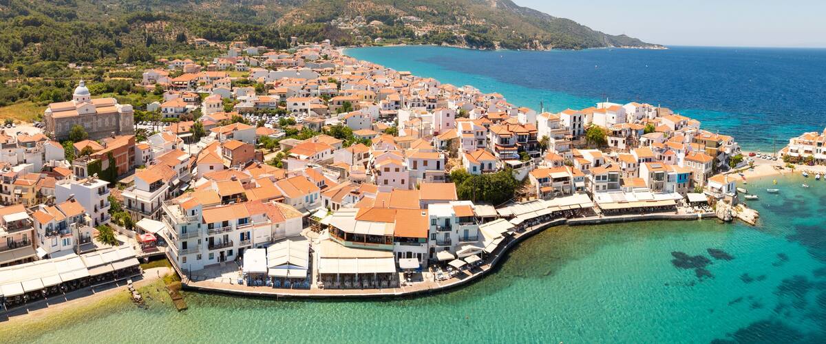A coastal town with white buildings, a clear blue sea, and a rocky peninsula.