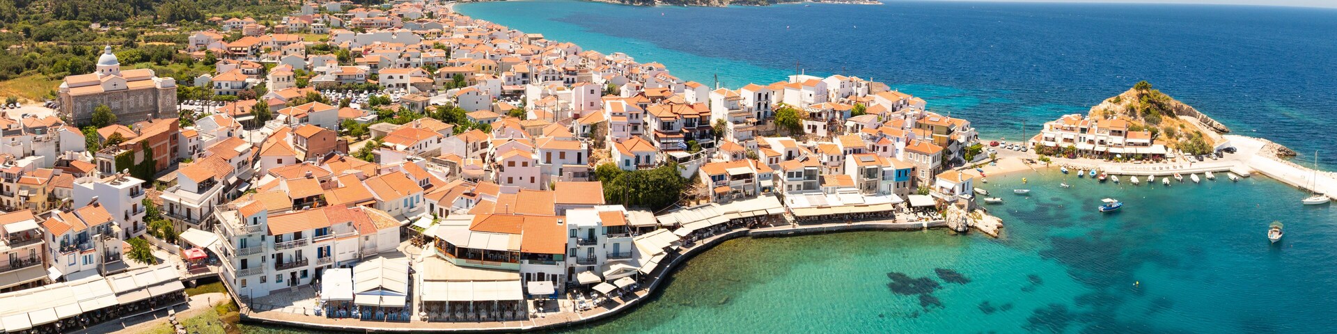A coastal town with white buildings, a clear blue sea, and a rocky peninsula.