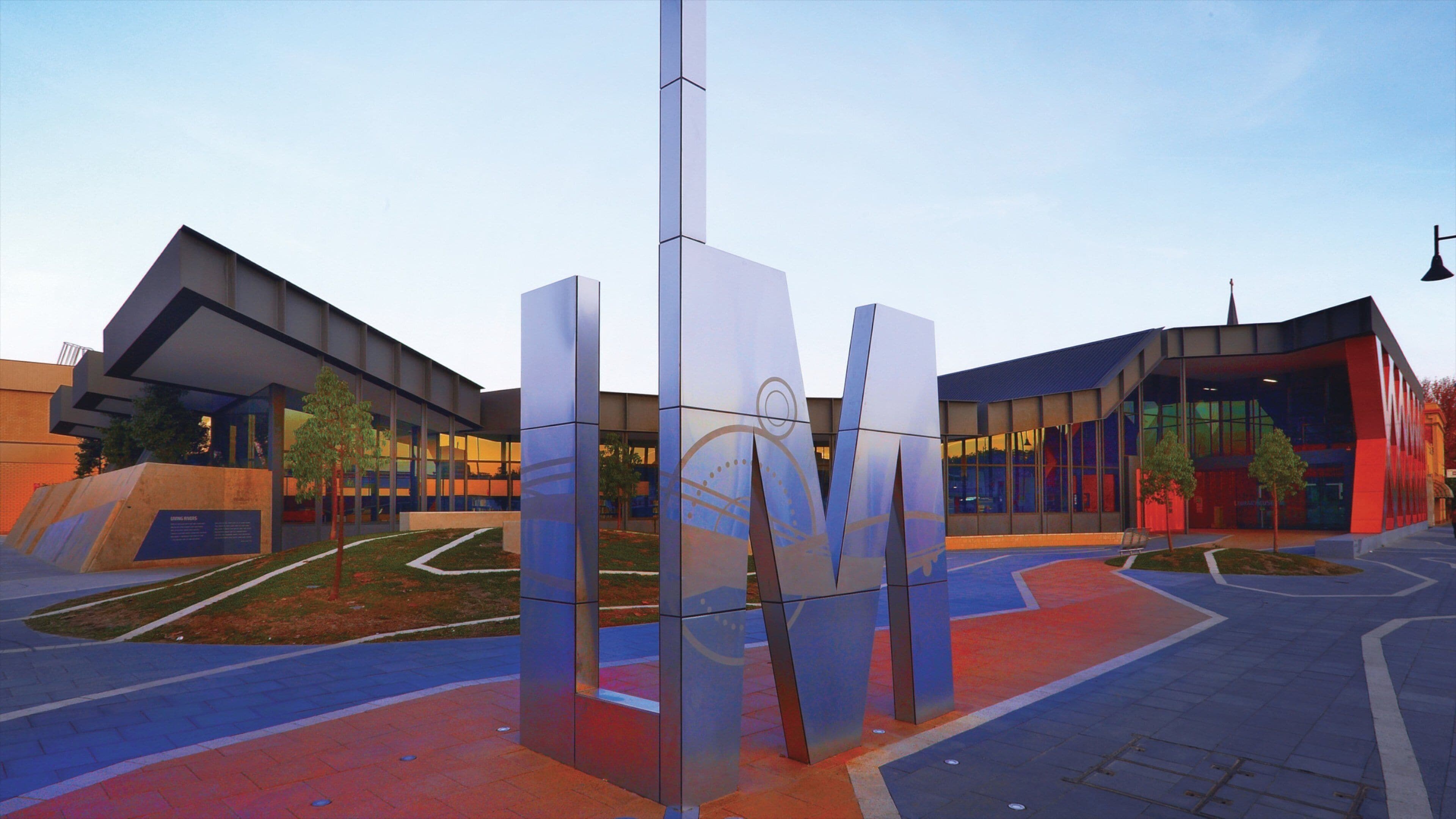 A modern building complex with reflective glass panels and a central sculpture.