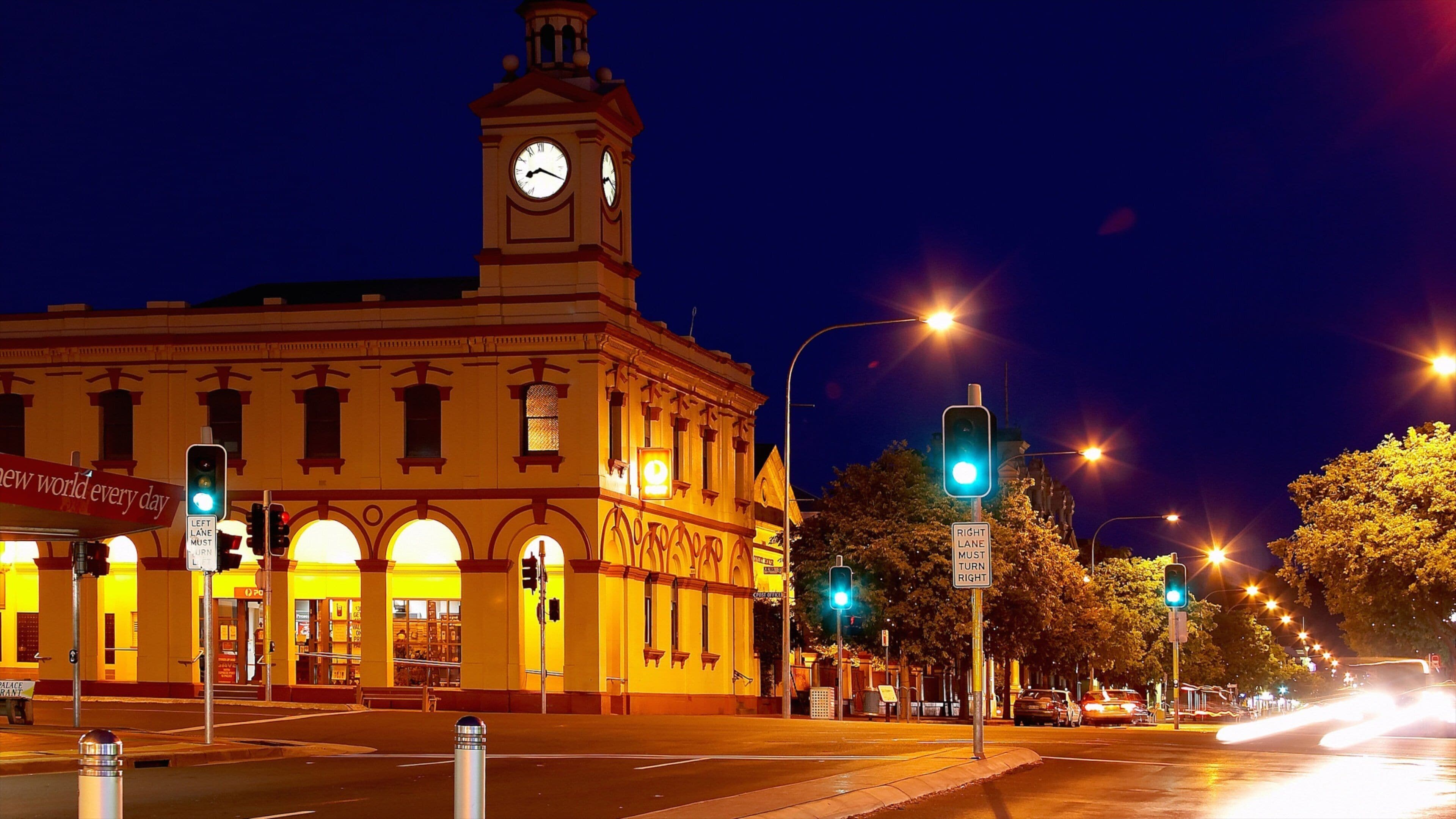 A historic building with a clock tower, illuminated streetlights, and traffic signals at a nighttime intersection.