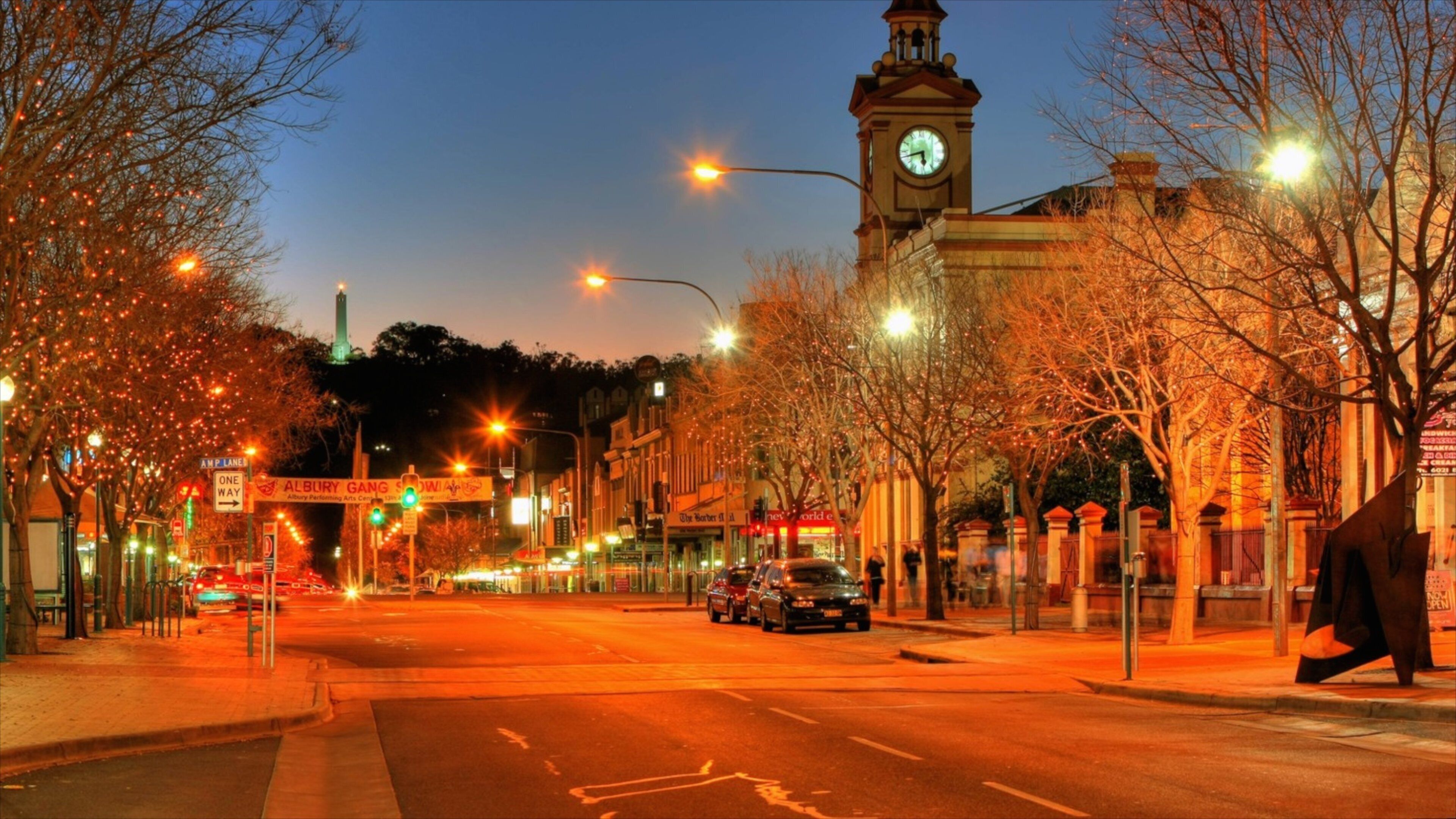 A street at dusk with a clock tower, illuminated trees, and a sign for the Albury Gang Show.