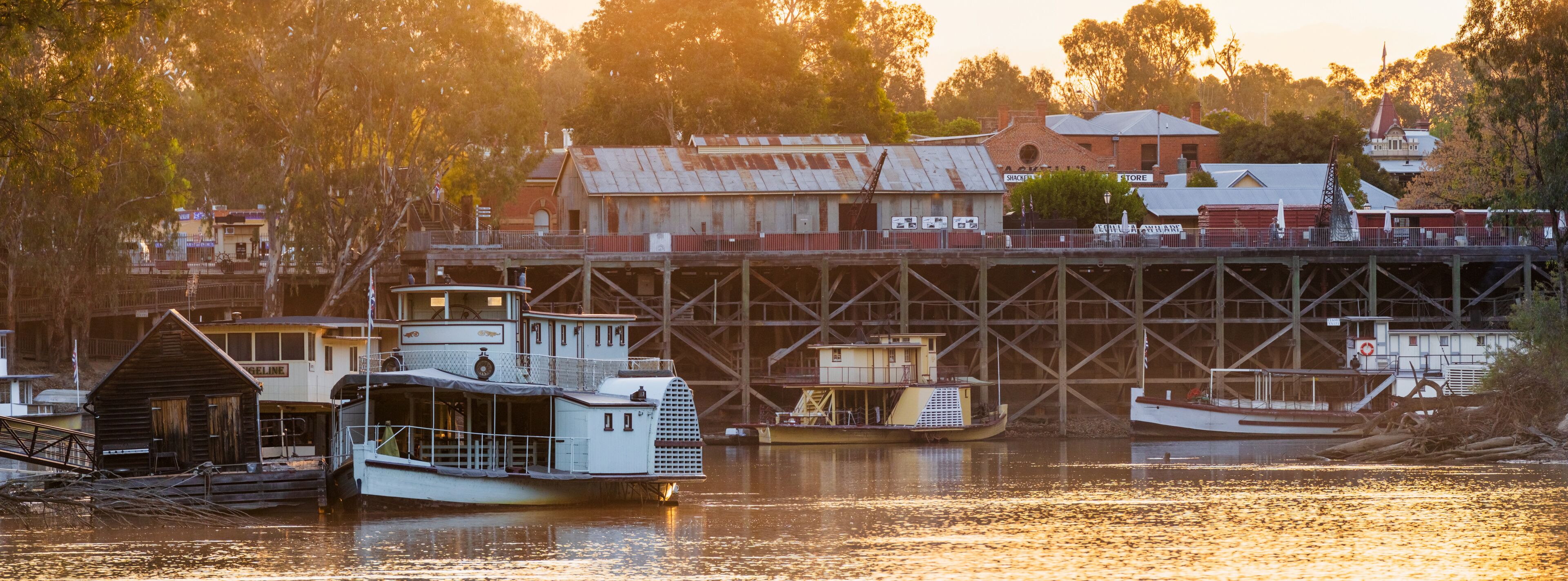 Panorma view of historic paddle steamers beside an old river port in golden evening light