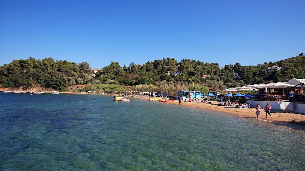 A clear coastal area with boats, a sandy beach, and buildings on a hillside.
